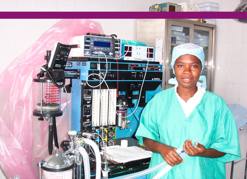 An old photo of SBH's early operating room, with a woman Haitian medical professional standing in front of anesthesia equipment