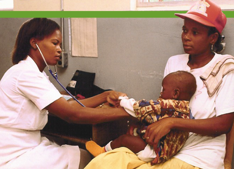 An old photo of a Haitian nurse using a stethoscope to check the heart beat of a young Haitian boy, who is sitting in his caregiver's lap. His caregiver is a Haitian woman.