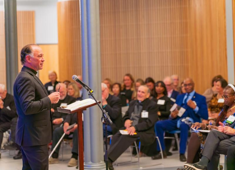 HEI Board Member Father John Unni speaks addresses attendees during the programatic portion of HEI's 2025 celebration.