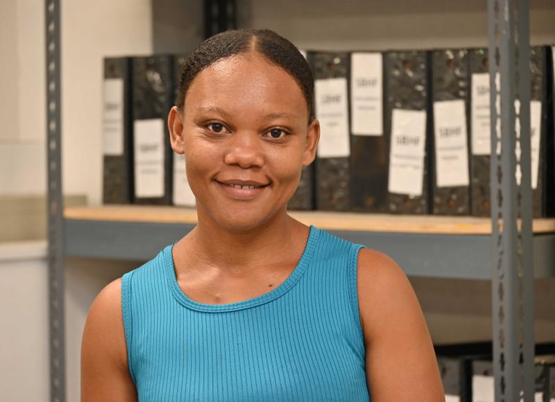 Portrait of a Haitian woman smiling. Her hair is parted and pulled back and she wears a blue tank top.