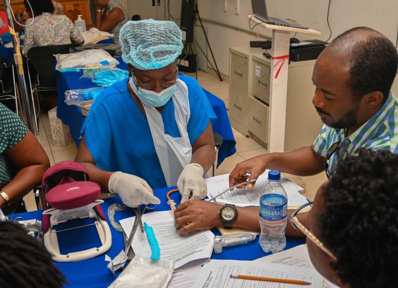 Clinicians sit at a table covered in papers and medical equipment as they engage in medical training.