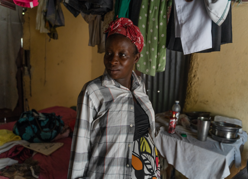 A Haitian woman stands proudly in her home and smiles. She looks to the side.