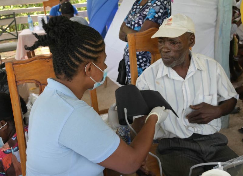 A community health nurse puts a blood pressure cuff on an elderly man at an earthquake mobile clinic.