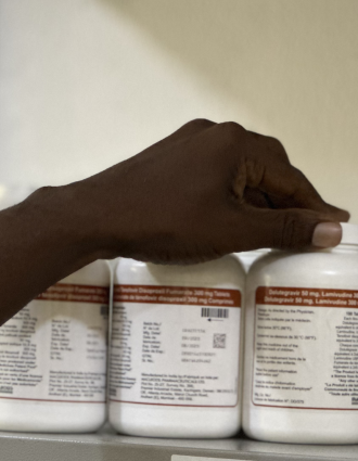 A Haitian hand reaching towards bottles of HIV medications on a supply room shelf.