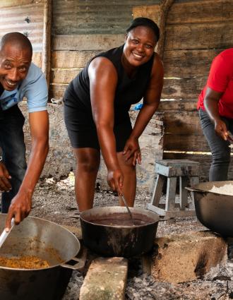 A man and two women stir large pots over charcoal fires at a Ti Fwaye session Lhomond, Haiti