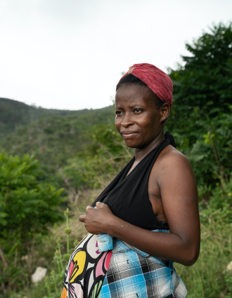 A Haitian woman stands in profile with her hands on top of her pregnant belly. She smiles and looks off into the distance.