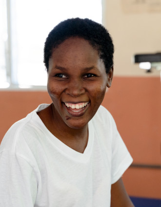 A Haitian woman smiles at the camera. She is shown from the waist up in a physical therapy office.
