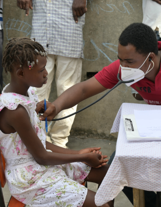 A doctor listens to a young girl's heart using a stethoscope at an earthquake mobile clinic.