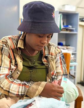A mother named Chery cradles her newborn baby in her lap, adjusting her baby's cap.