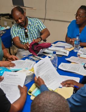 A group of Haitian clinicians are gathered around a table filled with papers and medical equipment.