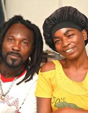 A Haitian man and woman sitting side by side, each leaning toward the other and smiling with great affection, openness, and warmth.