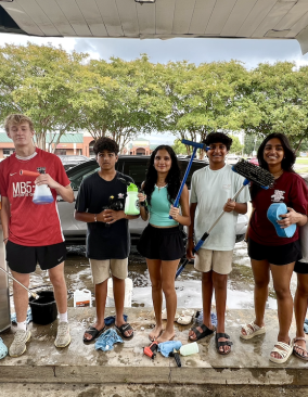 A group of high school students pose with car washing tools and equipment at their fundraiser.