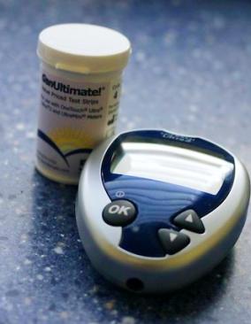 A small handheld diabetes glucometer and a cylindical container of testing strips sits on a speckled blue countertop.