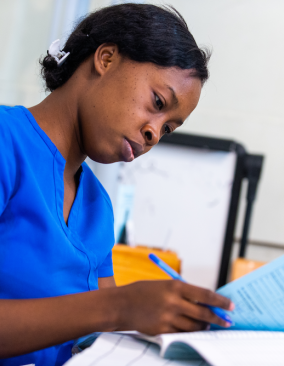 Sitting at a table, a Haitian nurse in bright blue scrubs studies a document she is holding.