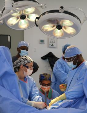 A group of surgeons in blue scrubs and face masks conduct a procedure.