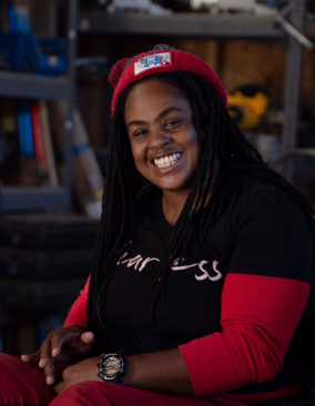 A Haitian woman sits in a wheelchair in an equipment workshop. She smiles brightly at the camera.