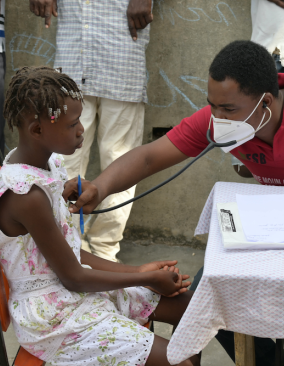 A doctor listens to a young girl's heart using a stethoscope at an earthquake mobile clinic.