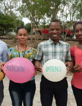 Four social workers, two men and two women, stand next to each other and smile at the camera. Each person holds a balloon with writing on it. The balloons says empathy, discretion, patience, and tolerance in French.