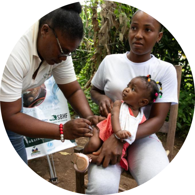 A community health wroker administeres a vaccine to a young girl, who is sitting in her mother's lap.