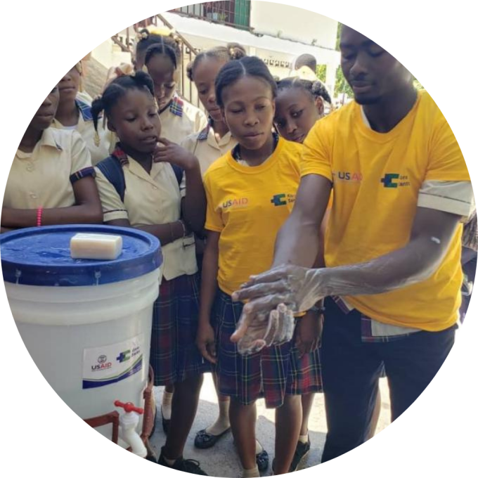 A community health worker teaches school children how to properly wash their hands.