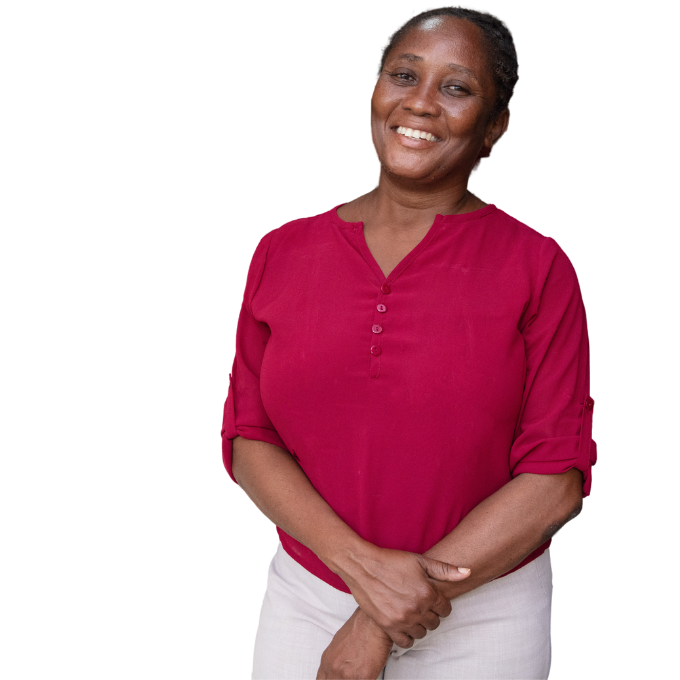 A Haitian doctor stands with her arms crossed at the wrist. She has a big smile on her face and wears a bright red shirt with buttons, sleeves rolled up. 
