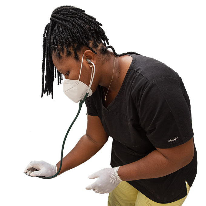 A woman Haitian doctor leans over with a stethescope in her hand. She wears her hair in braids, a black scrubs top, and a white medical mask.