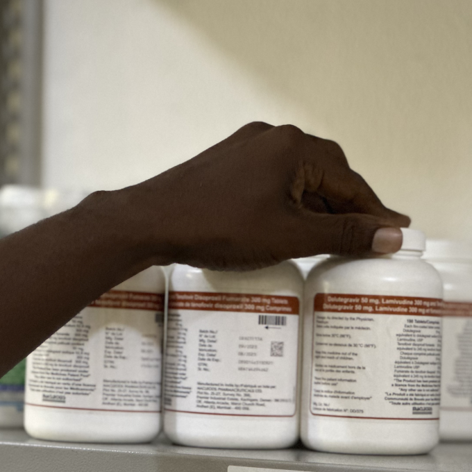 A Haitian hand reaching towards bottles of HIV medications on a supply room shelf.