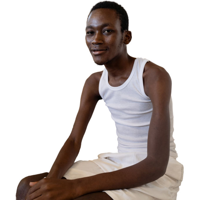 A Haitian man wearing a white tank top sits and smiles with his hand folded by his knees