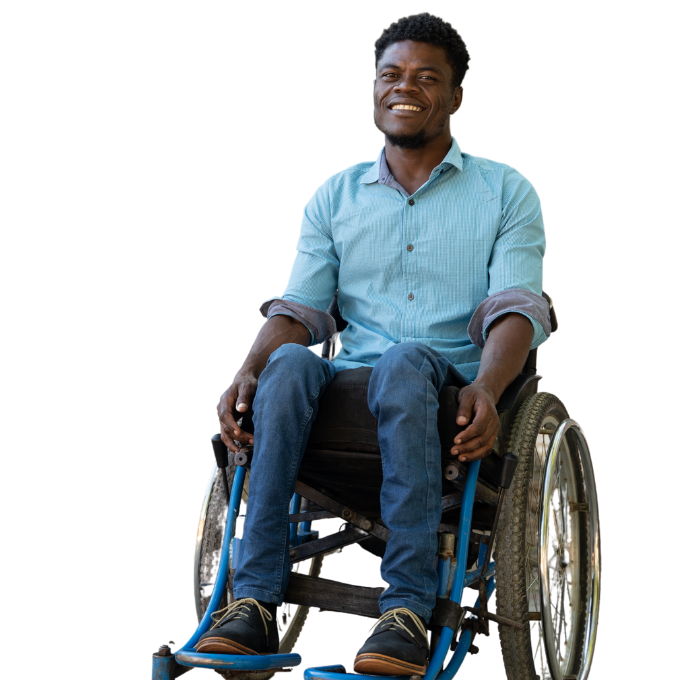 A Haitian man sits in a wheelchair and has a big smile on his face. He has short hair and is wearing blue jeans and a blue button-down shirt.