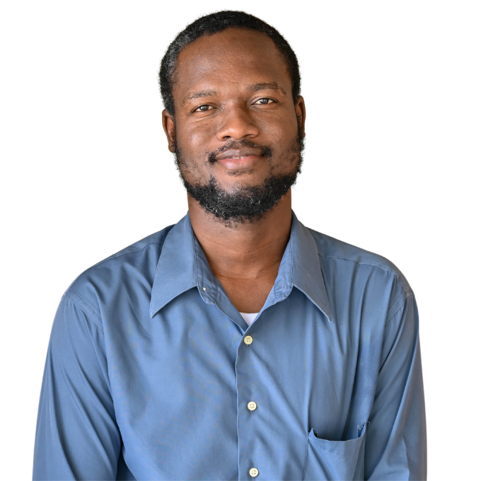 A portrait of a Haitian man with a beard, short hair, and a blue button down shirt smiling and looking straight ahead.